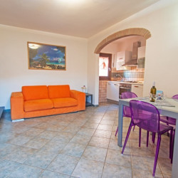 Zona giorno con divano arancione, tavolo con sedie e angolo cottura sullo sfondo
