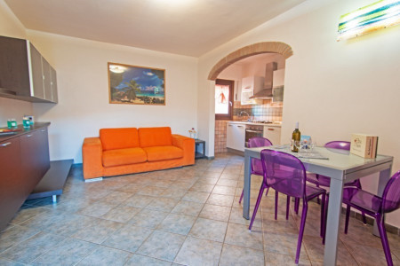 Zona giorno con divano arancione, tavolo con sedie e angolo cottura sullo sfondo
